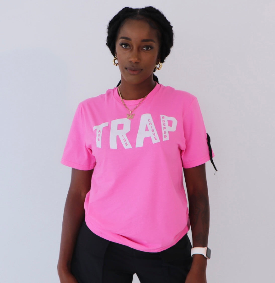 A person wearing a pink TRAP tee with a visible logo on the front with the words take risk achieve prosper standing against a white background