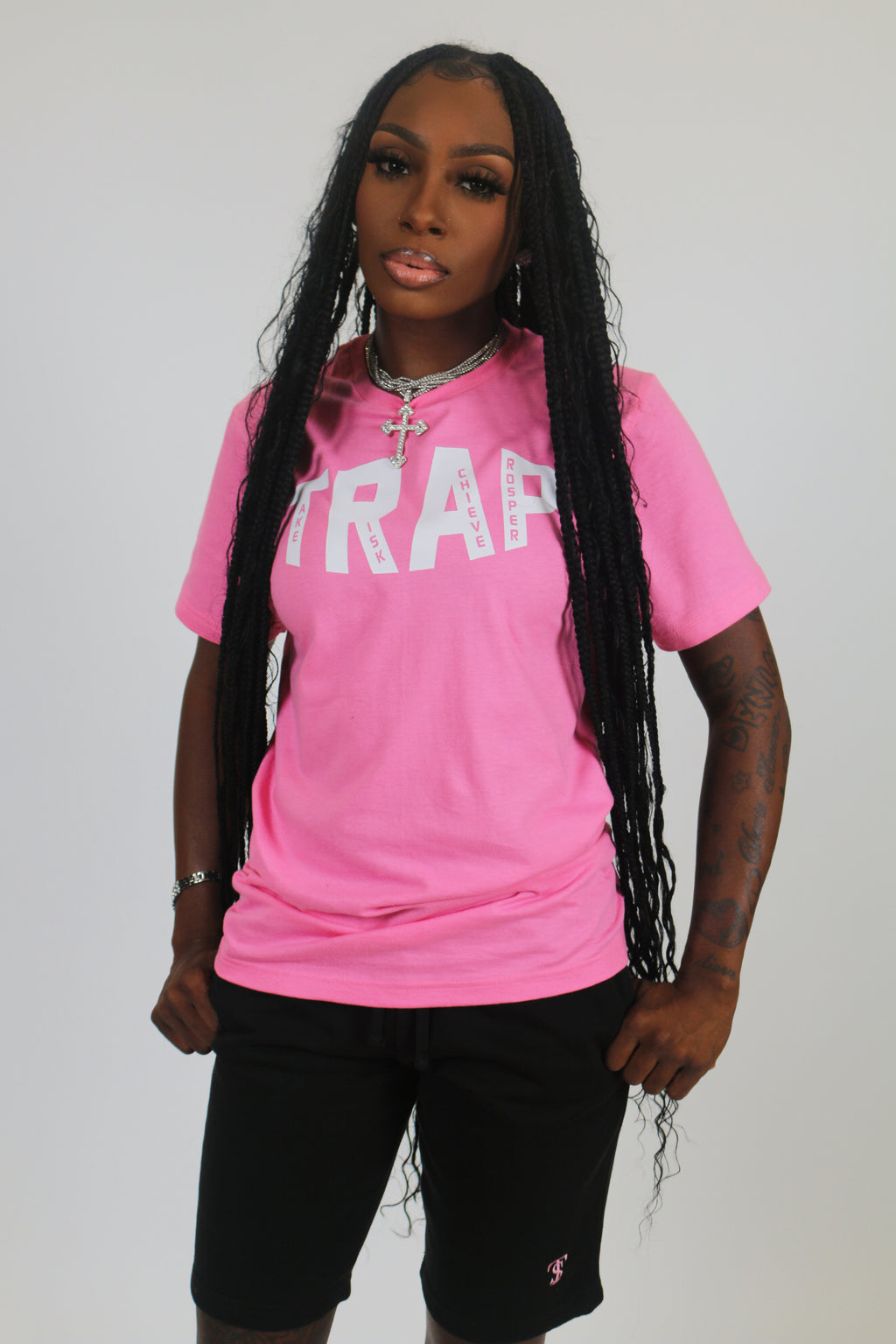 A person wearing a pink TRAP tee with a visible logo on the front with the words take risk achieve prosper standing against a white background